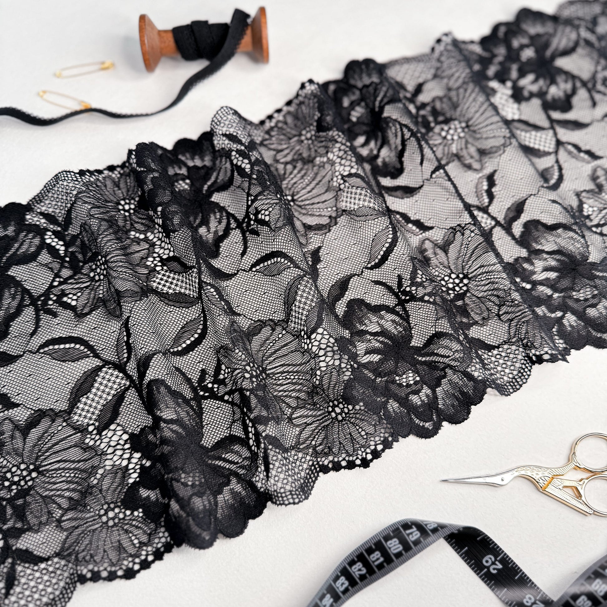 Black elastic lace fabric, 21 cm wide, featuring intricate floral patterns, displayed with sewing tools for lingerie crafting.