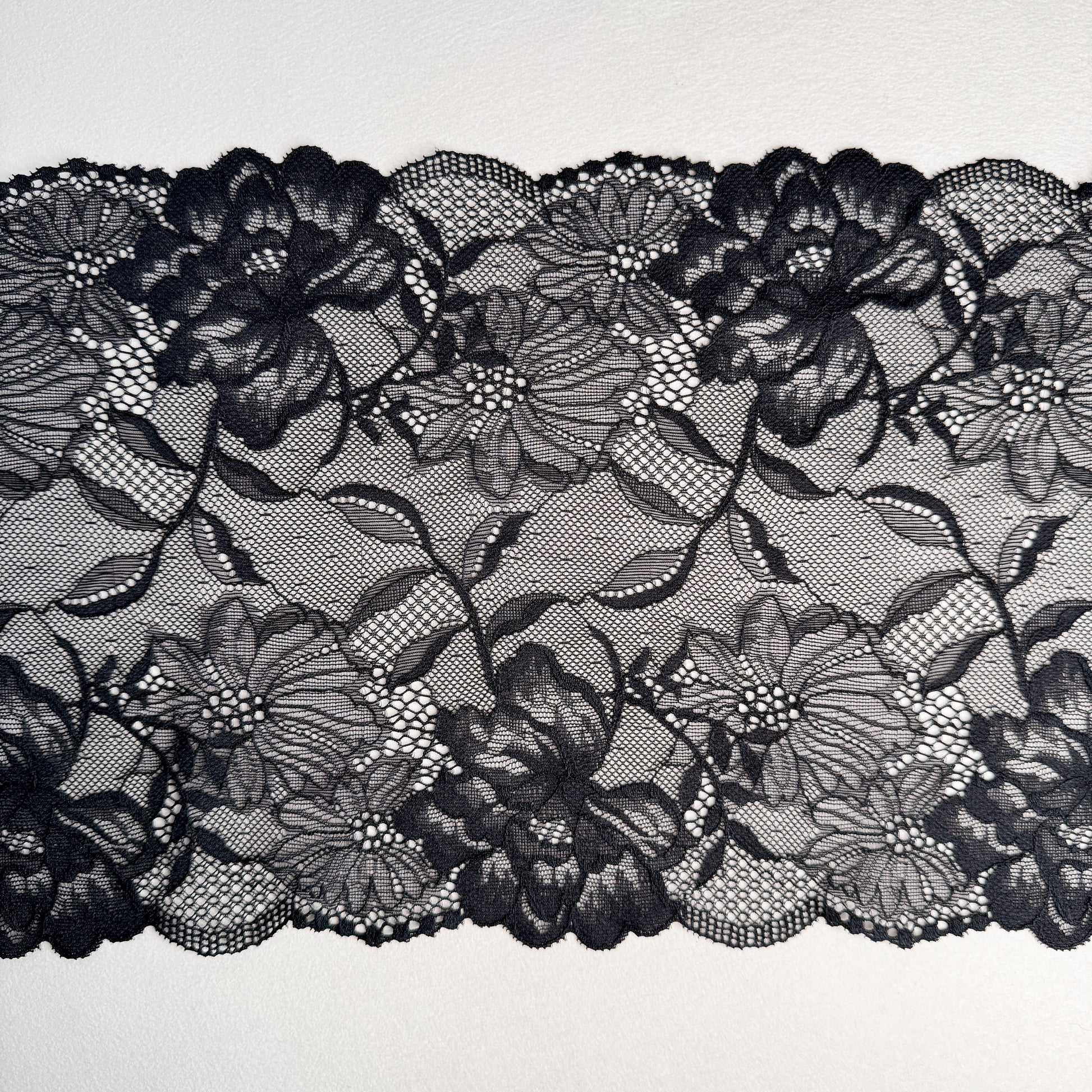 Close-up of black elastic lace, 21 cm wide, with delicate floral designs, perfect for sewing lingerie and other delicate garments.
