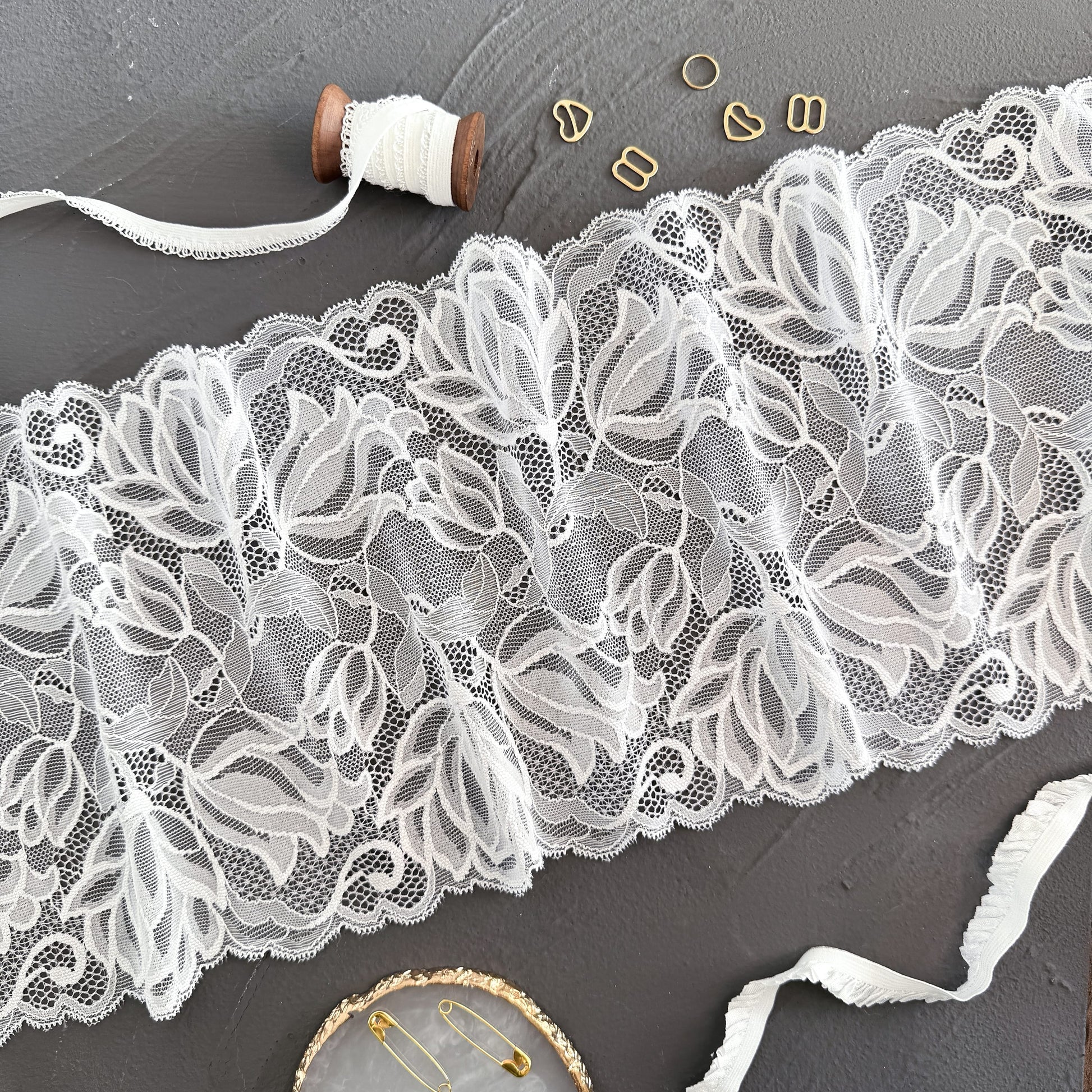 20cm wide white lace displayed with sewing accessories, showcasing its delicate and detailed floral patterns for lingerie making.