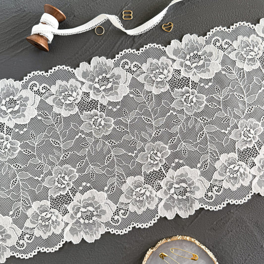 Off-white elastic lace fabric, 23 cm wide, laid flat to highlight its floral patterns and delicate craftsmanship, ideal for intimate apparel designs.