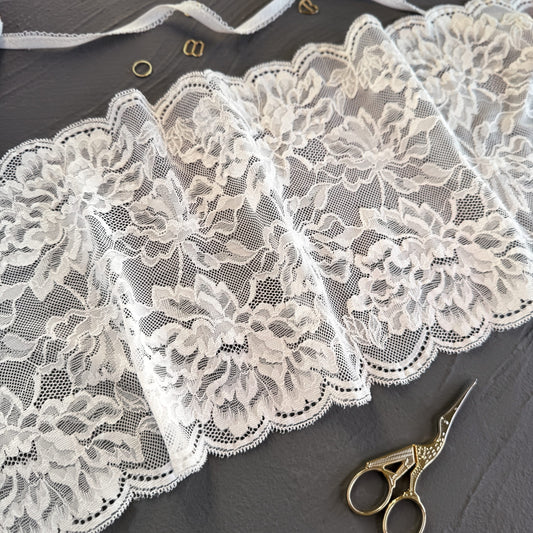 Milk elastic lace fabric, 22 cm wide, featuring delicate floral patterns, styled with gold sewing accessories on a dark gray background, ideal for lingerie making.