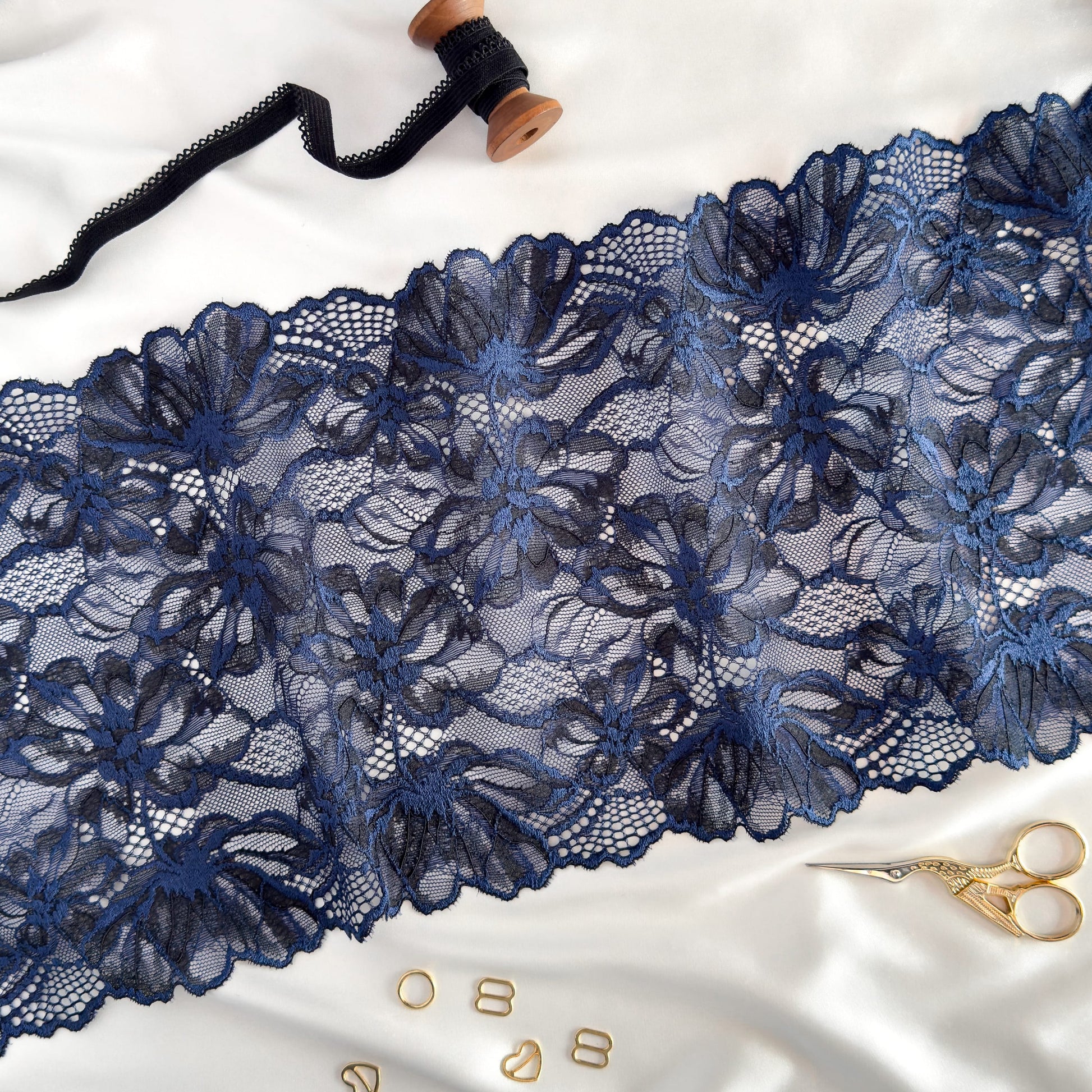 Dark blue elastic lace fabric, 22 cm wide, featuring intricate floral patterns, styled with sewing accessories for lingerie crafting inspiration.