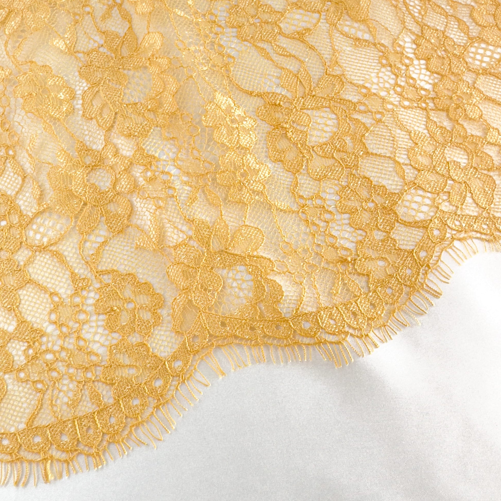 Close-up of mustard yellow Chantilly lace with intricate floral details and scalloped edges, perfect for lingerie and decorative crafts.