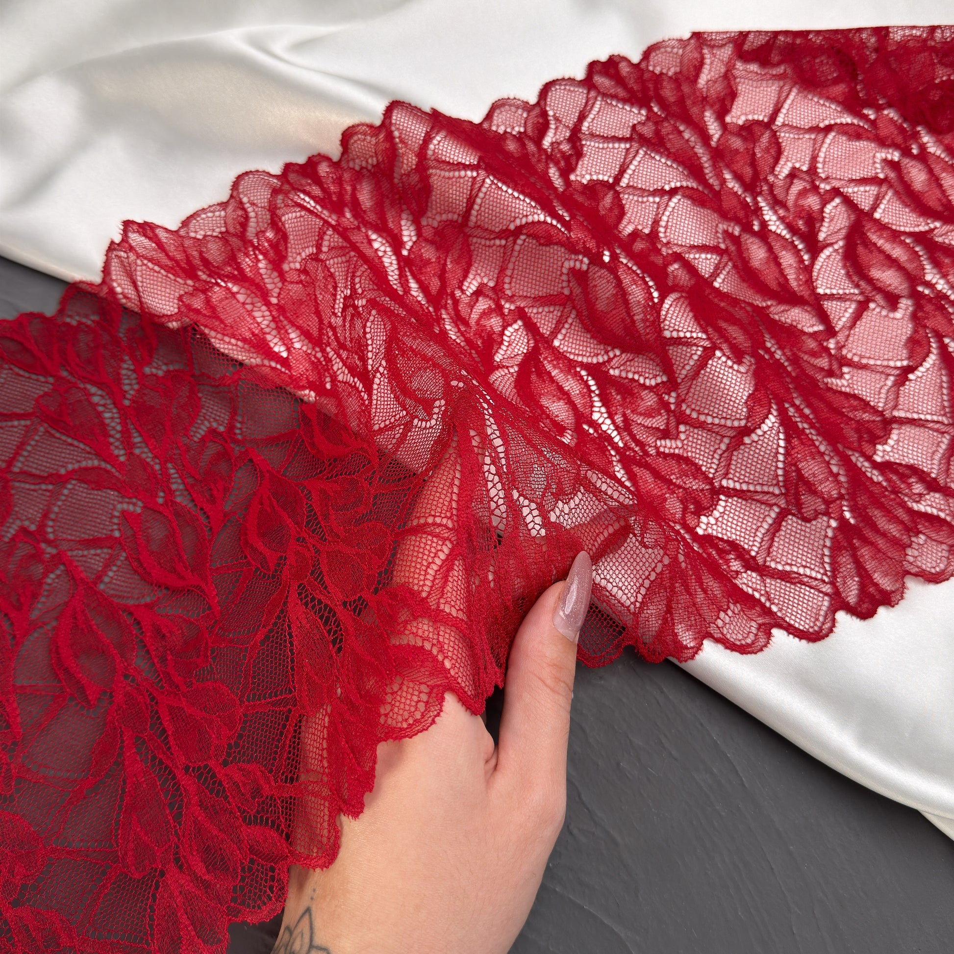 Red lace fabric held by a hand on a dark surface