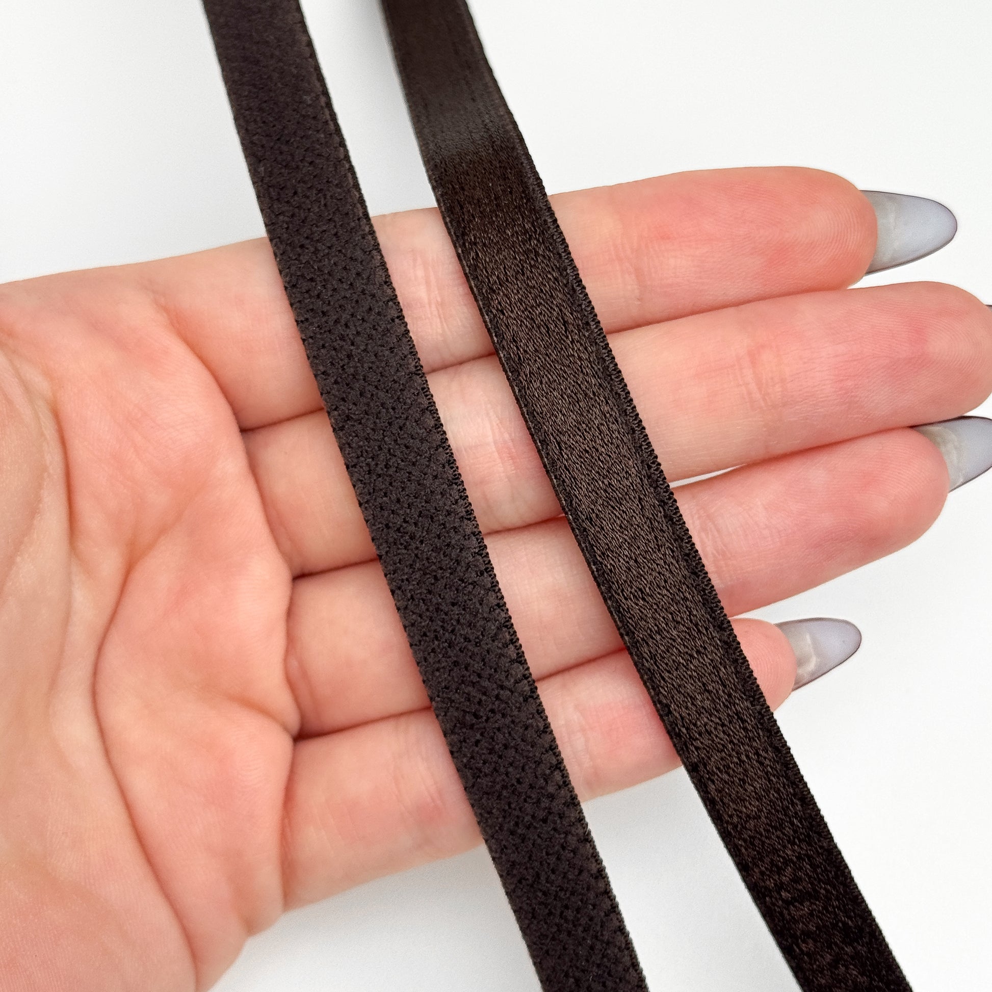 Two strips of brown elastic band held in a hand against a white background