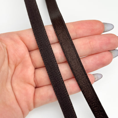 Two strips of brown elastic band held in a hand against a white background