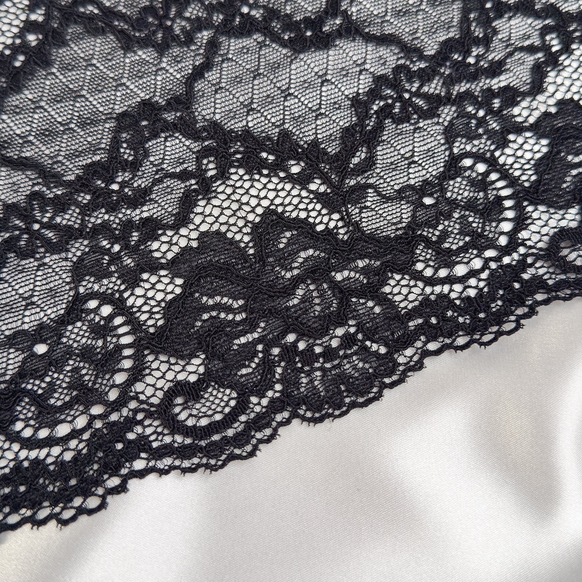 Close-up of black lace fabric on a white satin background