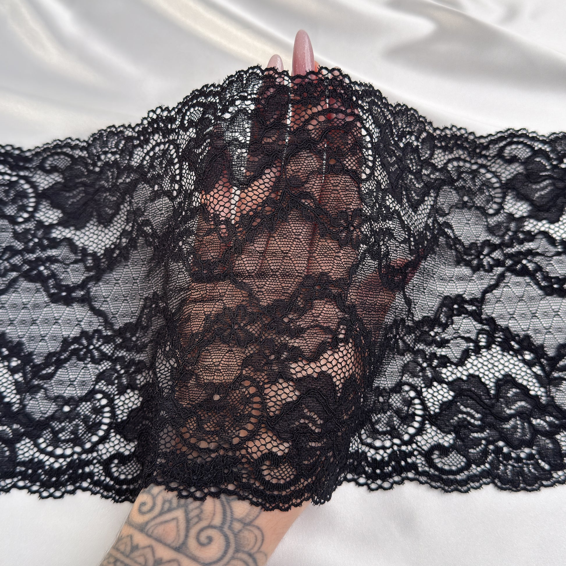 Black lace fabric held by a hand on a white background