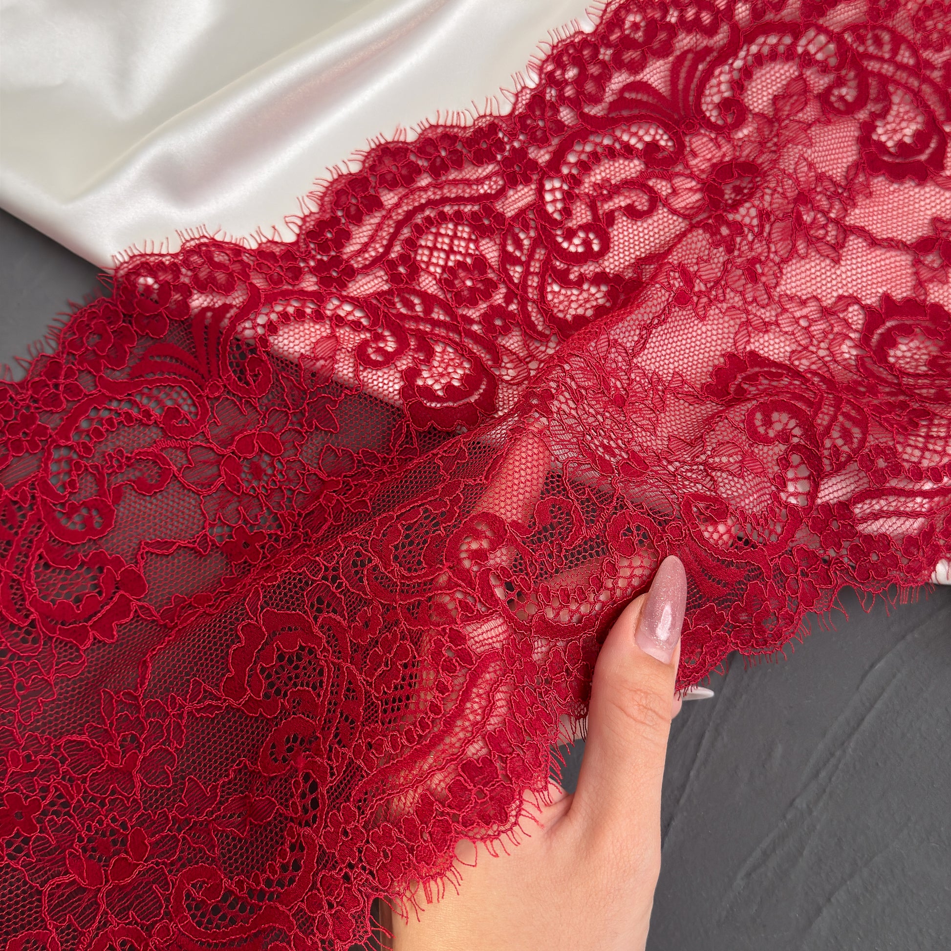 Red lace fabric held by a hand on a gray background